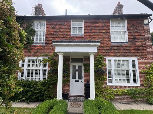 Before Traditional brick house with white windows and a front porch, surrounded by greenery.